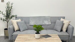 A grey sofa with patterned cushions, a wooden coffee table, a potted plant, and a small side table with a lamp. - Modern 3bedroom Home in Bury Premium Mattresses Blackout Blinds Ensuite M (Bury)