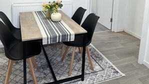A dining area with a table, chairs, a radiator, a door, and a poster on the wall. - Modern 3bedroom Home in Bury Premium Mattresses Blackout Blinds Ensuite M (Bury)