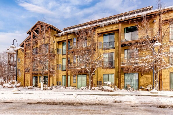 A multi-story building with balconies, large windows, and a snow-covered ground. - Plush condo with pool, gym, hot tubs, garage & central AC - snowbird-friendly (Heber City)
