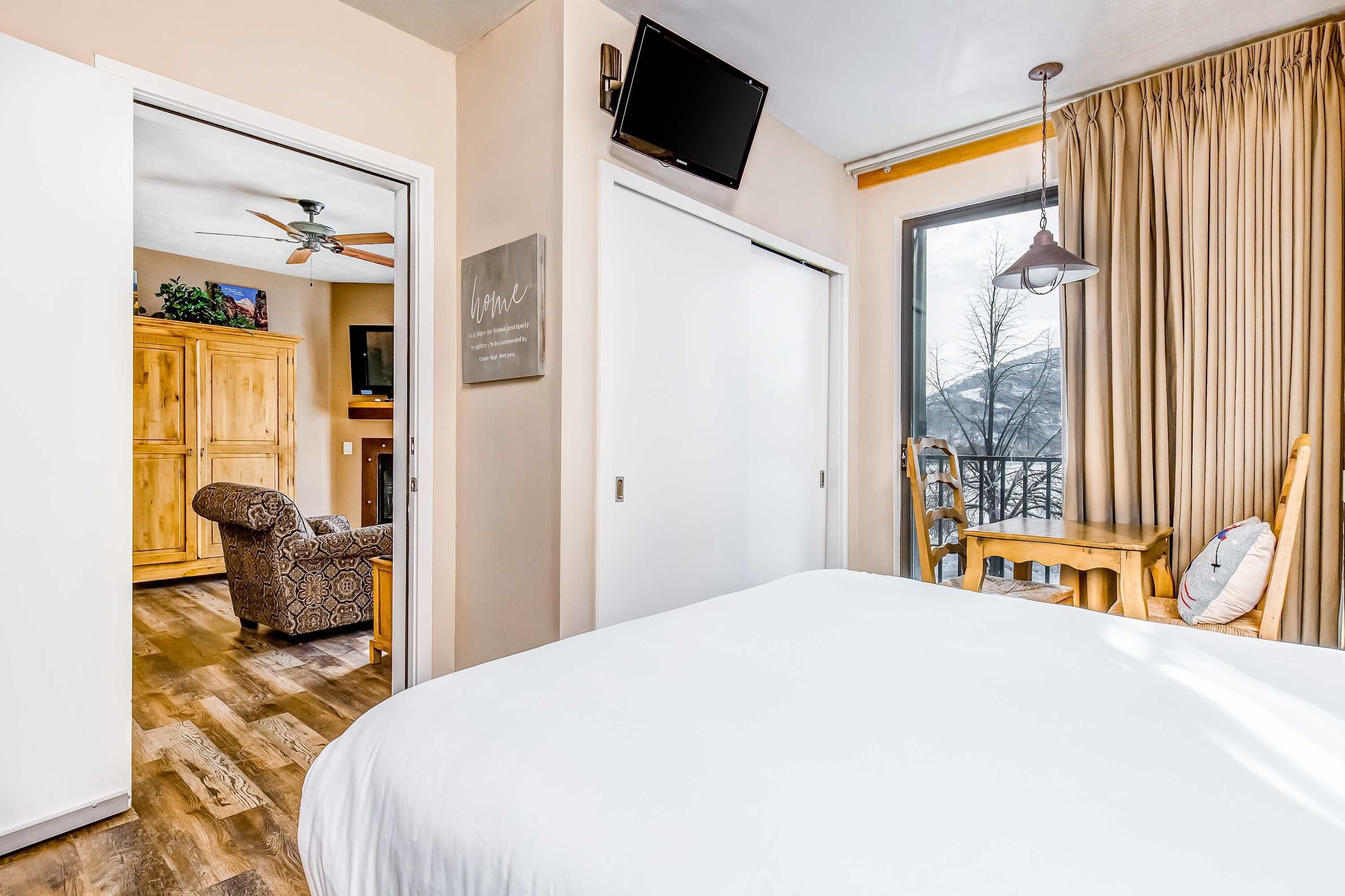 Une chambre d’hôtel équipée d’un lit, d’une télévision, d’une chaise, d’une table, d’un ventilateur de plafond et offrant une vue sur l’extérieur.