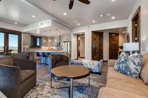 A spacious living area with a round coffee table, sofas, and a kitchen in the background. - Luxury condo with large deck, pool/hot tub, walk to ski access (Park City)