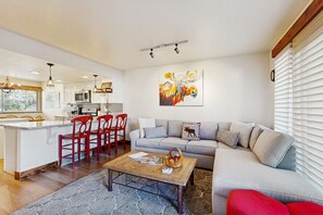A modern kitchen with white cabinets, a dining area with red chairs, a gray sofa, and a coffee table with magazines. - Cheery townhome in Park City with large, furnished deck & private hot tub (Park City)