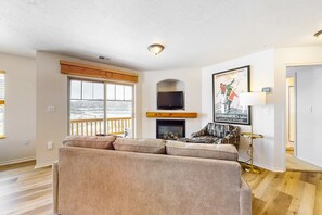 A living room with a sofa, a fireplace, a television, and a poster on the wall. - Amazing lake view condo with  fireplace, balcony, shared pool & hot tub (Heber City)