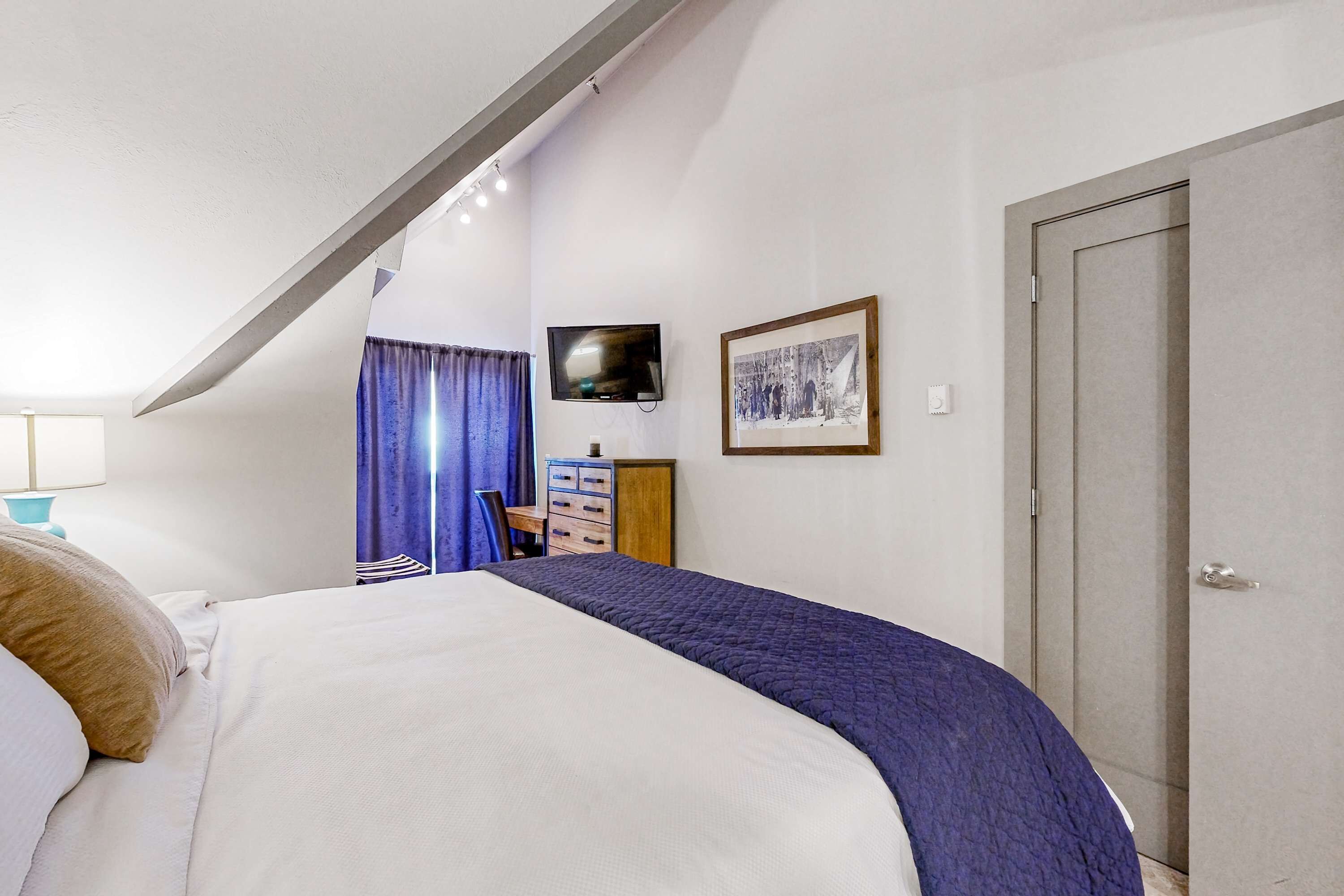 A bedroom with a bed, a dresser, a television, and a door.