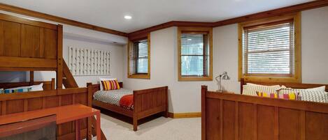 A bedroom with two wooden beds, a desk, and a chair.