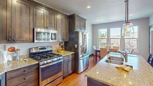 A modern kitchen with stainless steel appliances, wooden cabinets, granite countertops, and a dining area with natural light. - Spacious townhome with pool, private hot tub & clubhouse - Dog Friendly (Kamas)