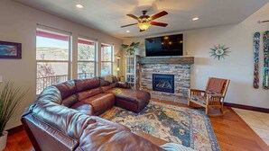 A living room with a leather sectional sofa, a fireplace, a ceiling fan, and a large window. - Spacious townhome with pool, private hot tub & clubhouse - Dog Friendly (Kamas)