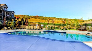 A swimming pool with lounge chairs, a building with a sign, and a hilly landscape in the background. - Spacious townhome with pool, private hot tub & clubhouse - Dog Friendly (Kamas)