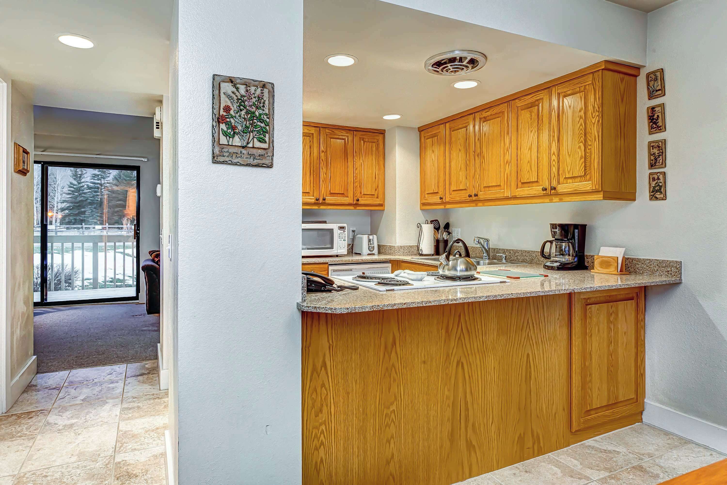 A kitchen with wooden cabinets, a granite countertop, and a view to a balcony.
