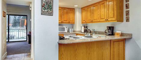 A kitchen with wooden cabinets, a granite countertop, and a view to a balcony.