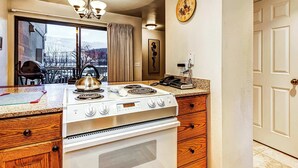 A kitchen with a stove, oven, wooden cabinets, a chandelier, and a clock on the wall. - Modern condo with spectacular views - close to top ski resorts & walk to MARC (Park City)
