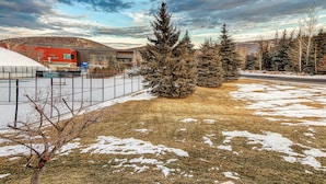 A fenced outdoor area with snow patches, a building with a red facade, and evergreen trees. - Modern condo with spectacular views - close to top ski resorts & walk to MARC (Park City)