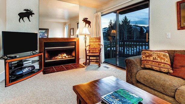 A living room with a fireplace, a television, a sofa, and a view through a sliding glass door. - Modern condo with spectacular views - close to top ski resorts & walk to MARC (Park City)