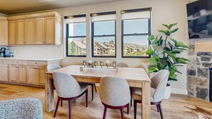 A modern kitchen with wooden cabinets, a dining table with chairs, and a large window with a view of buildings. - Lakeview Condo with fireplace, gas grill & W&D - close to skiing, hiking, & lake (Heber City)