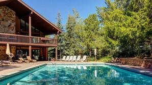 A pool with lounge chairs, a stone building, and trees in the background. - Modern mountain escape with wonderful views, pool, hot tub-minutes to skiing (Park City)