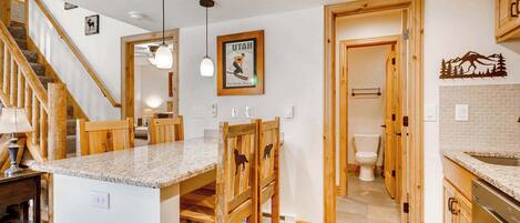 Una cocina con armarios de madera, encimera de granito, una mesa de comedor de madera y una escalera.