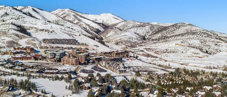 Un pueblo cubierto de nieve con una combinación de edificios residenciales y comerciales, incluyendo un hotel destacado con un telesilla visible al fondo.