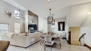 A modern living room with a sectional sofa, a dining table with chairs, a stone accent wall, and a mounted deer head. - Three King Suites, 12 min to Deer Valley & Park City Resorts (Kamas)