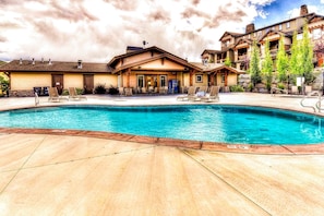 A pool area with lounge chairs, a building with a covered patio, and a mountainous backdrop. - Three King Suites, 12 min to Deer Valley & Park City Resorts (Kamas)