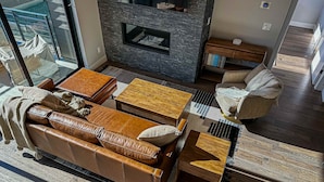 Een moderne woonkamer met een open haard, een leren bank, een houten salontafel en een glazen deur naar een buitenruimte.