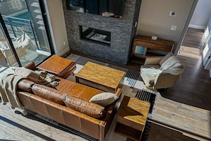 A modern living room with a fireplace, leather sofa, wooden coffee table, and a glass door leading to an outdoor area. - Stunning house with  ski & lake views, private hot tub, private W&D (Hideout)