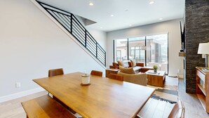 Een moderne woonkamer met een houten eettafel, een trap en een groot raam.
