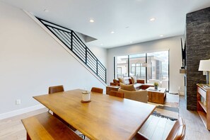 A modern living room with a wooden dining table, a staircase, and a large window. - Stunning house with  ski & lake views, private hot tub, private W&D (Hideout)