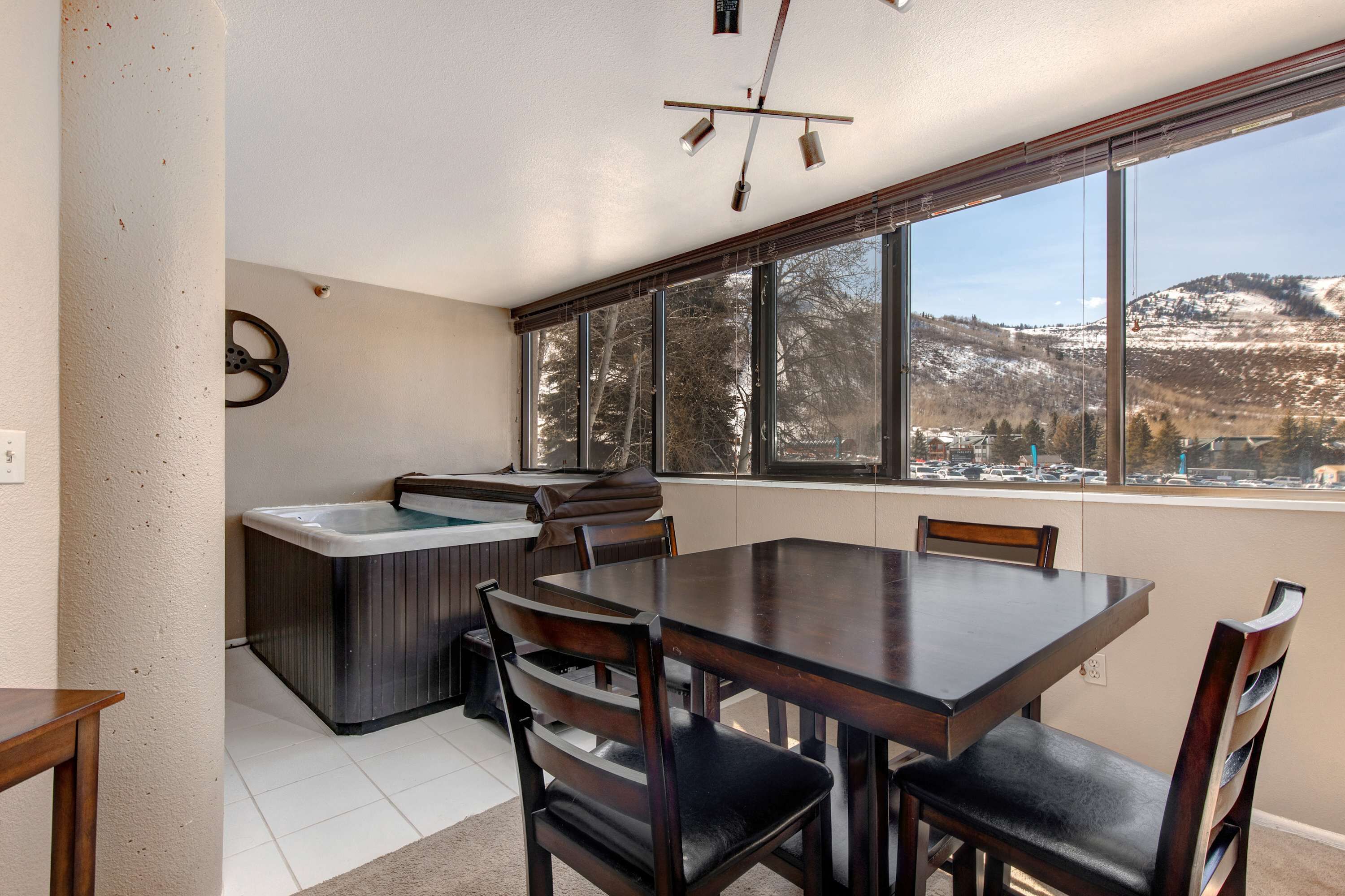 Un coin repas avec une table et des chaises, un jacuzzi et une grande fenêtre donnant sur les montagnes.