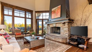 Una sala de estar amplia con chimenea de piedra, ventanas grandes, un televisor de pantalla plana y una zona de estar acogedora.