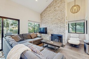 A modern living room with a stone wall, a flat-screen TV, a fireplace, a sofa, and a white chair. - Modern mountain townhouse with incredible views, hot tub & pool, & walk to lifts (Park City)