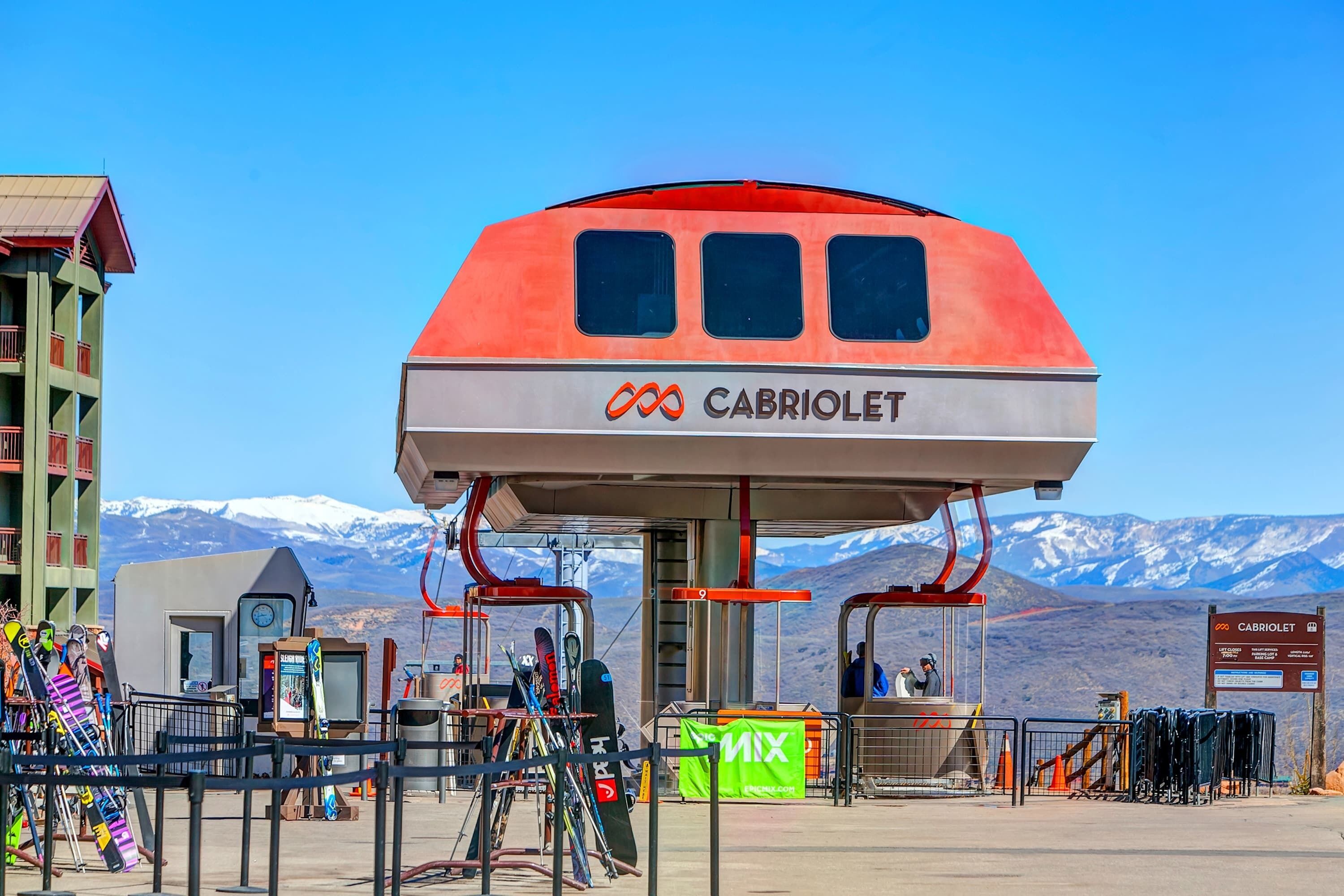 Estação de teleférico com um letreiro chamativo 'CABRIOLET', suporte para esquis e um cenário montanhoso.