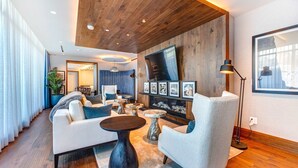 Ein modernes Wohnzimmer mit Sofa, Sessel, rundem Couchtisch und einem an der Wand montierten Flachbildfernseher.