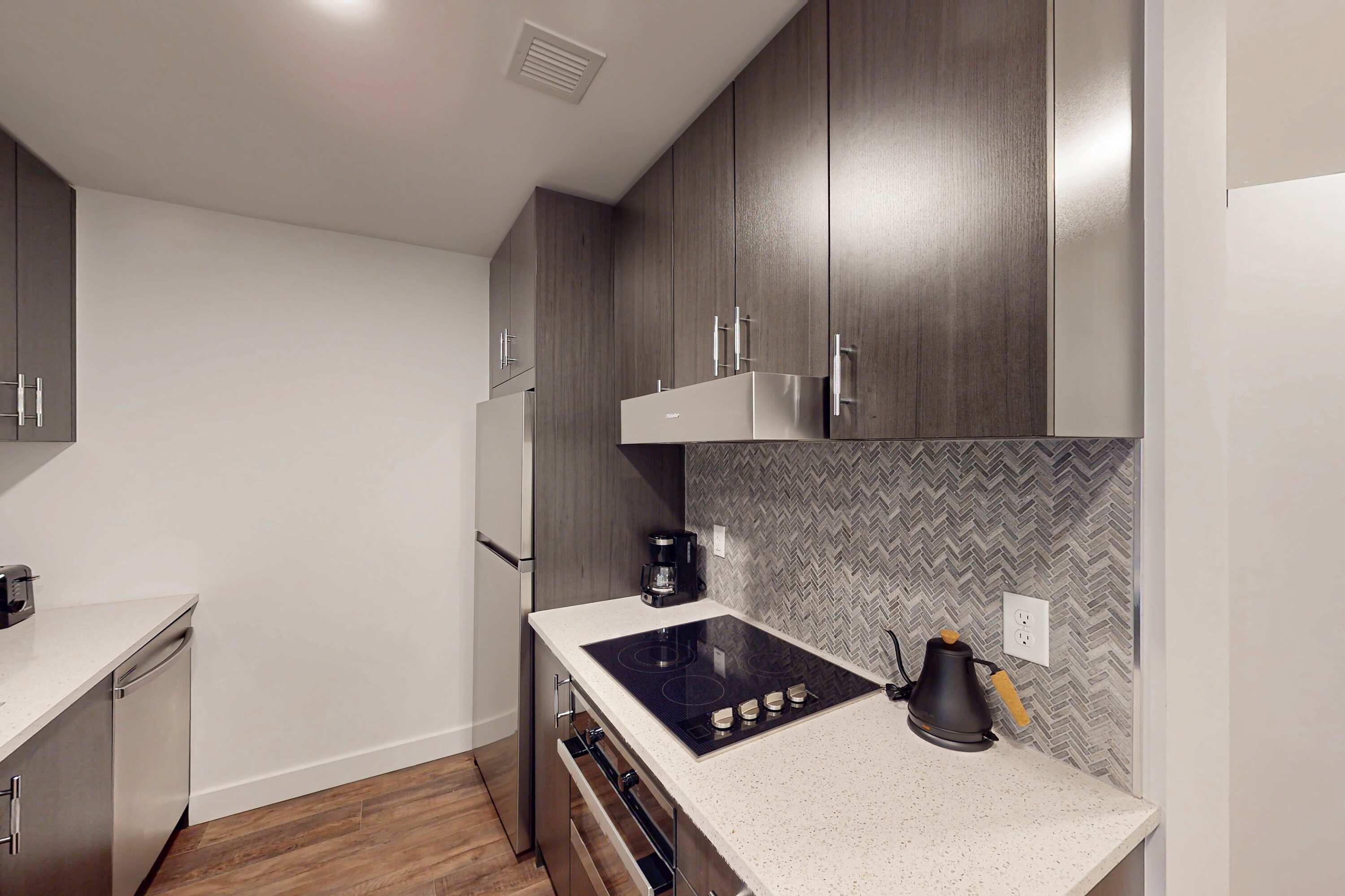 A modern kitchen with wooden cabinets, a white countertop, a built-in stove, and a herringbone-patterned backsplash.