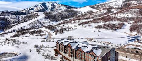 A hotel with a modern design, situated in a snowy mountainous area with a ski slope nearby.