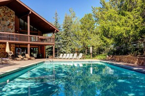 Ein Pool mit Liegestühlen, ein Steinhaus und Bäume im Hintergrund.