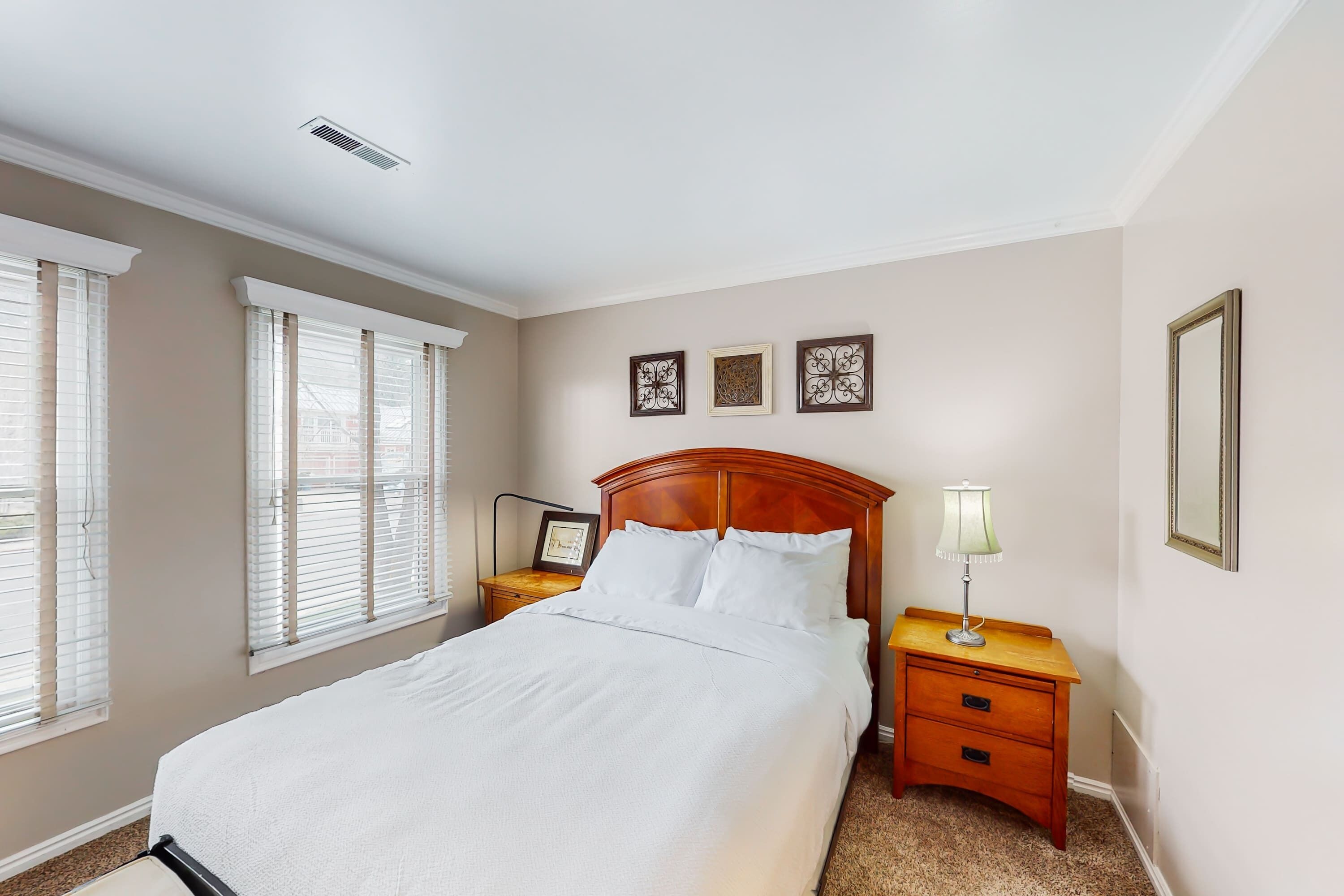 A neatly made bed with white linens, a wooden headboard, and a nightstand with a lamp.
