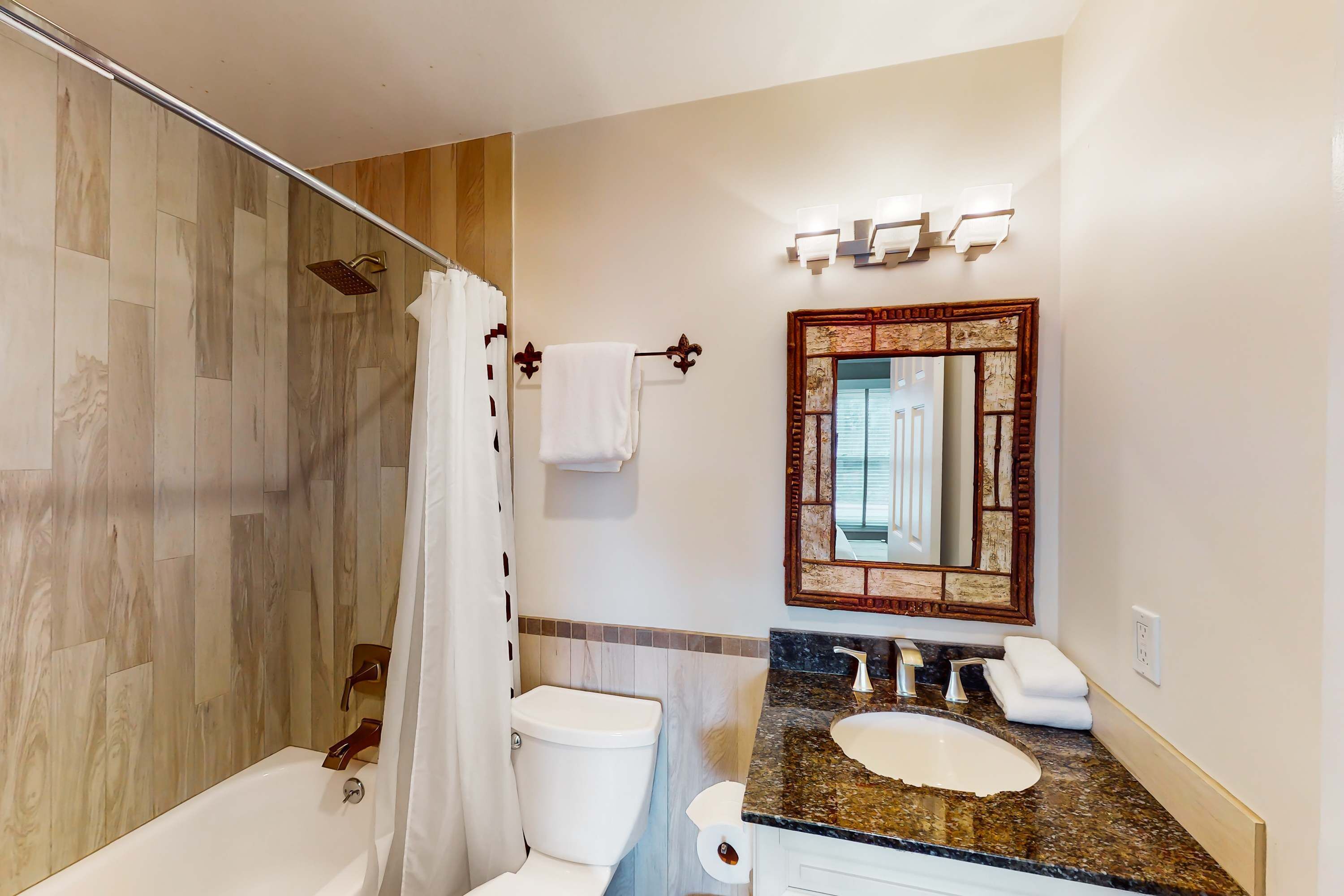 A bathroom with a shower, toilet, sink, and a mirror with a decorative frame.
