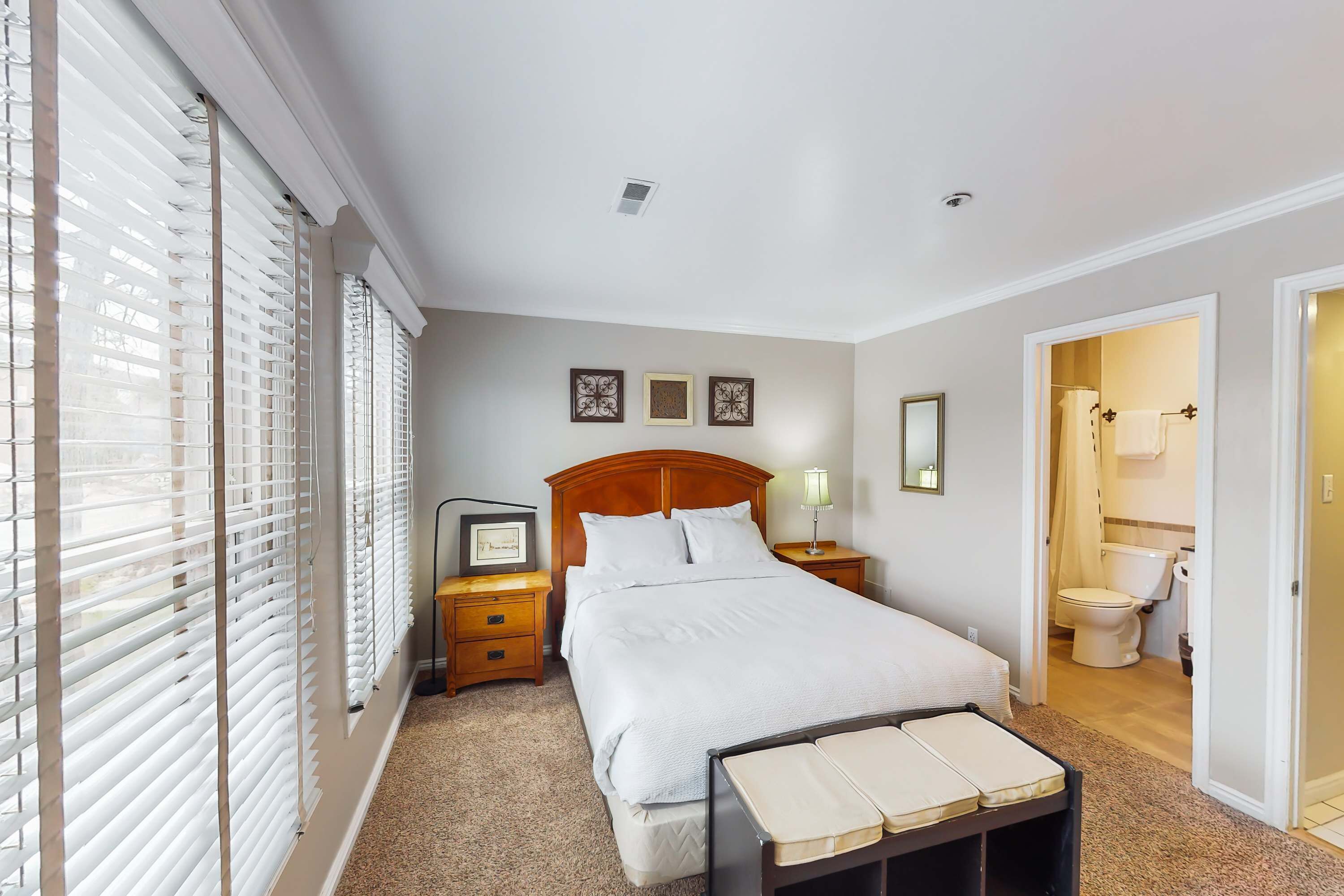 A bedroom with a large bed, a bedside table with a lamp, a TV, and a window with blinds.