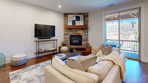 A living room with a stone fireplace, a flat-screen TV, a sofa, and a large window with a view. - Spacious townhouse with community pool, balcony & gym - close to Hideout (Hideout)