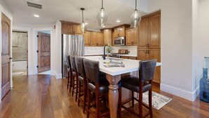 A kitchen with wooden cabinets, a central island, bar stools, pendant lights, a refrigerator, a microwave, and a sink. - Spacious townhouse with community pool, balcony & gym - close to Hideout (Hideout)