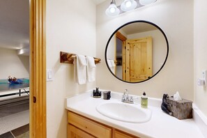 A bathroom with a white sink, wooden vanity, a round mirror, and a towel rack. - Beautiful ski chalet with gourmet kitchen, theater room & private hot tub (Brighton)