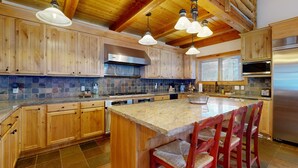 A kitchen with wooden cabinets, a large island with bar stools, stainless steel appliances, and a stone backsplash. - Beautiful ski chalet with gourmet kitchen, theater room & private hot tub (Brighton)