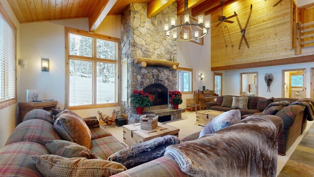 A cozy living room with a stone fireplace, plaid sofas, and a ceiling fan. - Beautiful ski chalet with gourmet kitchen, theater room & private hot tub (Brighton)