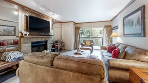 Een woonkamer met een open haard, een televisie, een bank en een balkon met uitzicht.