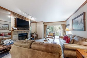 A living room with a fireplace, a television, a sofa, and a balcony with a view. - Mountain escape with pool, hot tub & balcony - near town lift & Main St (Park City)