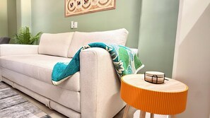 A beige sofa with a teal throw blanket, a small wooden side table with a yellow lampshade, and a green wall with a framed artwork. - Rooftop pool + mountain view
Sleeps 6 Family-Friendly Stay in PV (Puerto Vallarta)