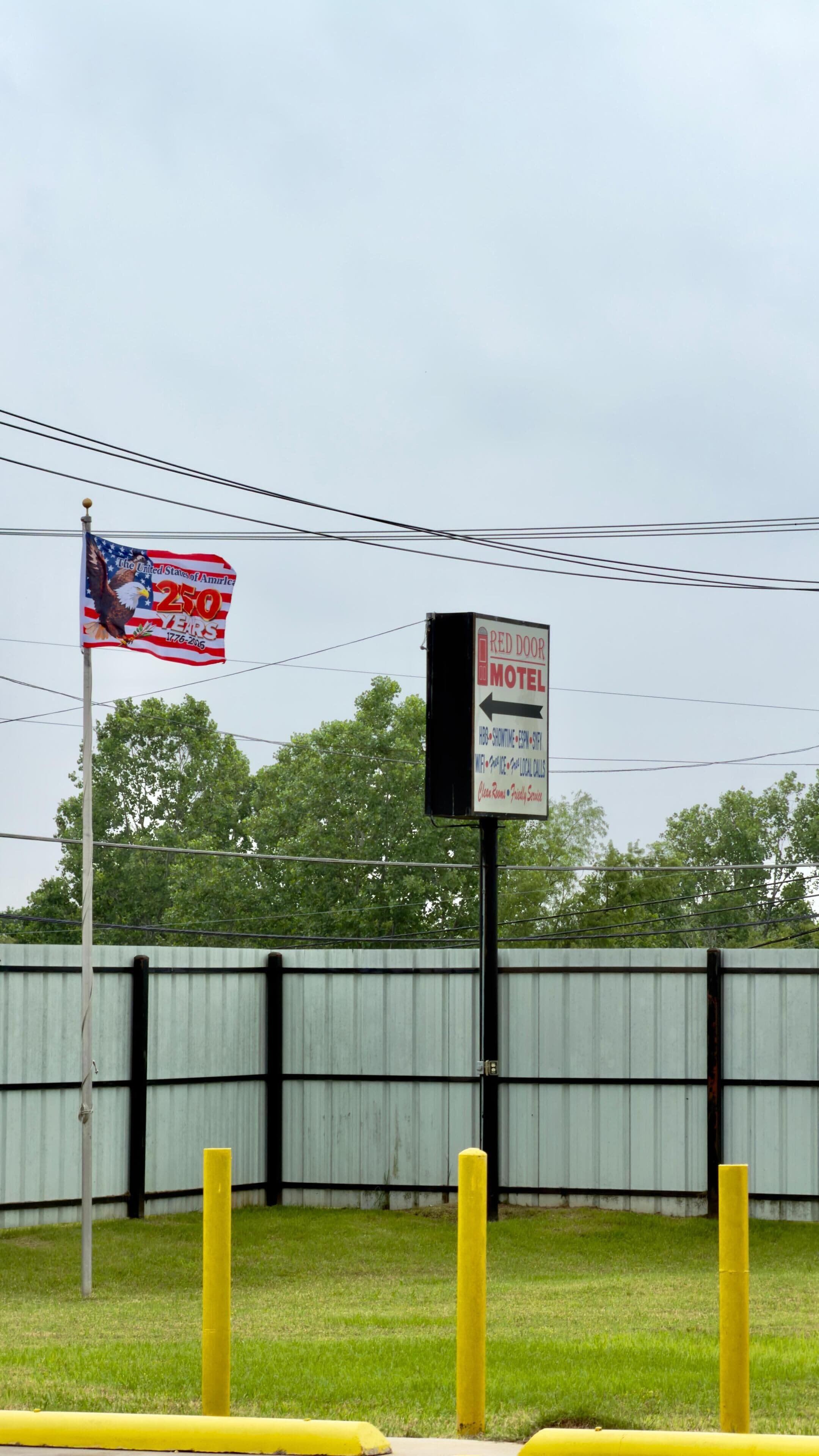 A motel sign with a directional arrow, a flagpole with a flag, and a metal fence in the background.