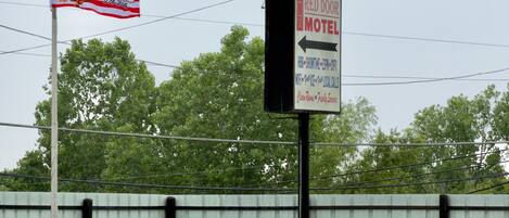 A motel sign with a directional arrow, a flagpole with a flag, and a metal fence in the background.