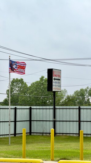 A motel sign with a directional arrow, a flagpole with a flag, and a metal fence in the background. - RED DOOR MOTEL (Dallas)