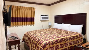 Une chambre d’hôtel avec un grand lit, un téléviseur fixé au mur, une petite table avec un téléphone et une fenêtre avec des rideaux.